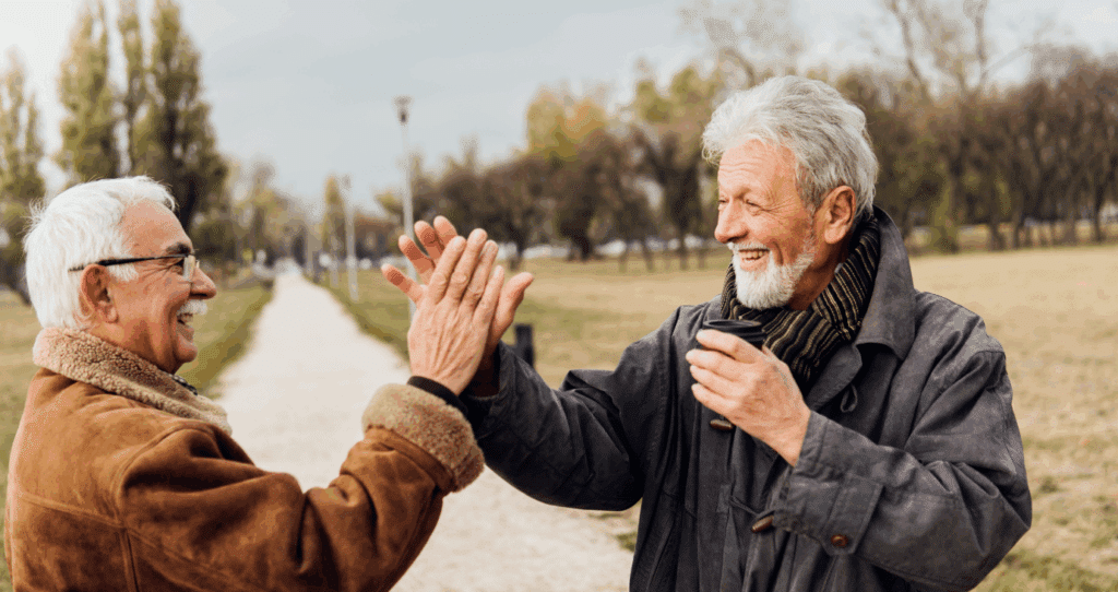 Zwei ältere Männer begrüßen sich herzlich bei einem Spaziergang im Park.