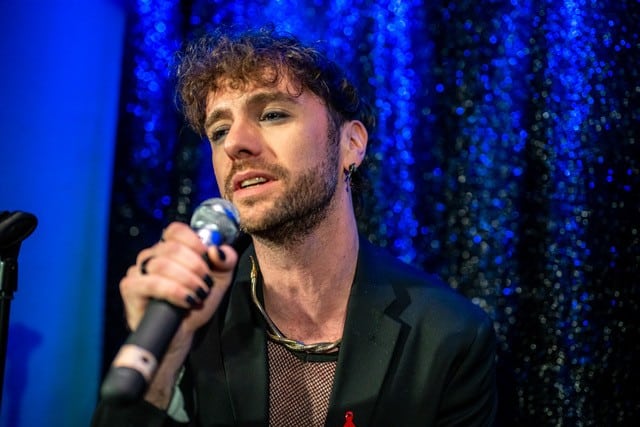 Ein Sänger performt live auf der Bühne beim Charity-Abend „Together for Hope“ in Hamburg, mit Mikrofon und blauer Bühnenbeleuchtung im Hintergrund.