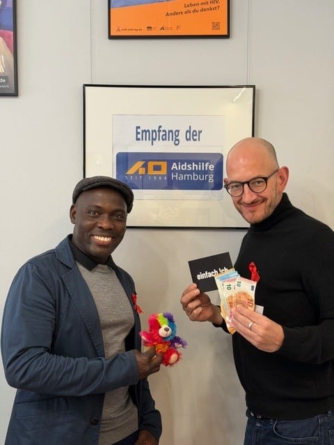 Torsten Poggenpohl (rechts) steht mit einem Teilnehmer beim Charity-Abend und zeigt ein Buch sowie ein kleines Geschenk, beide lächeln in die Kamera.