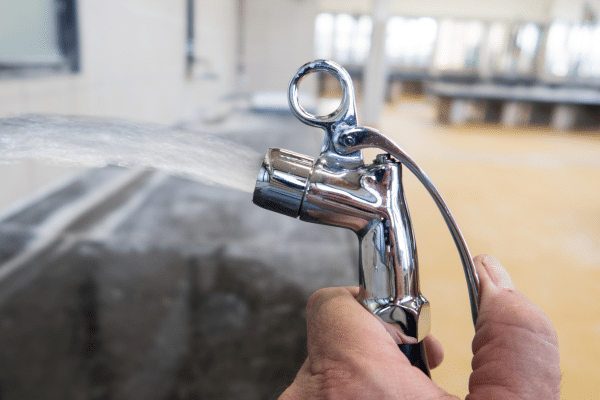 Hand hält eine Analspülung beziehungsweise Handdusche an einem Waschbecken.