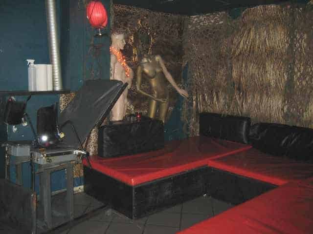 Dunkler Clubraum mit roten Sitzflächen, schwarzem Sofa, Dekoration und gedämpftem Licht.