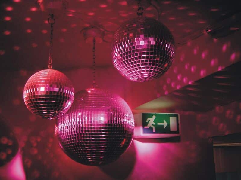 Mehrere Discokugeln hängen in einem Clubraum mit rotem und pinkem Licht.