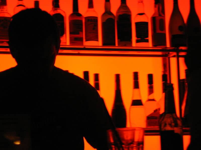 Silhouette einer Person in einer Bar mit Flaschen und warmem Licht im Hintergrund.