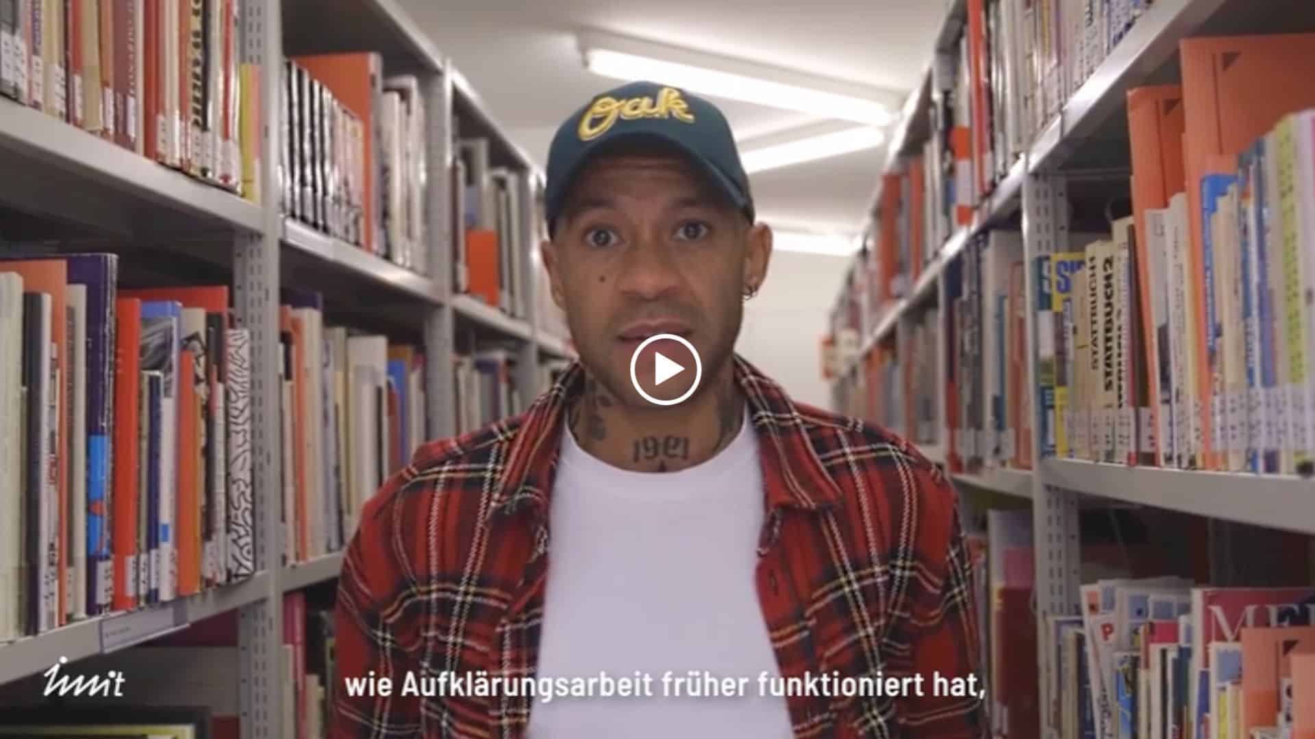 Jonathan Gregory, IWWIT-Kampagnenleiter und Mitinitiator von Druck machen!, im Projektfilm vor Bücherregalen. Zum Abspielen anklicken.