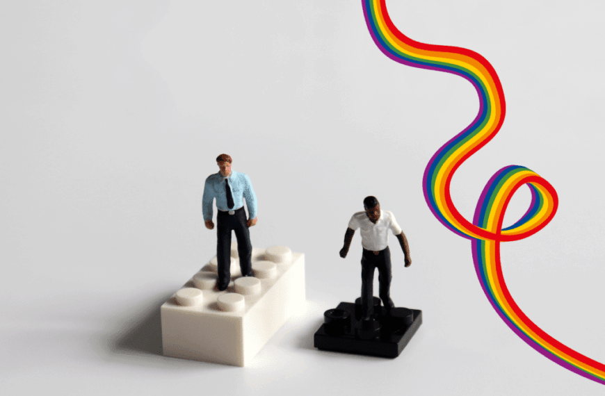 Zwei Spielfiguren auf getrennten Sockeln mit Regenbogenlinie dazwischen – Symbol für Ausgrenzung in queeren Communities.
