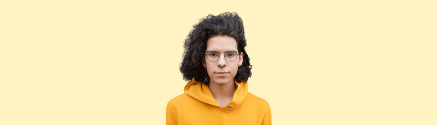 Lizzy - young trans woman with long curly hair in a yellow hoodie against a light background