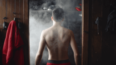 Rückansicht eines Mannes mit Handtuch vor der dampfenden Sauna im Fitnessstudio