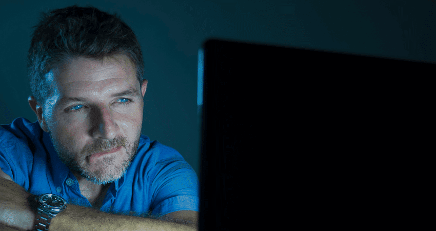 A man sits in front of a screen at night and watches intently - symbolising the consumption of pornography.