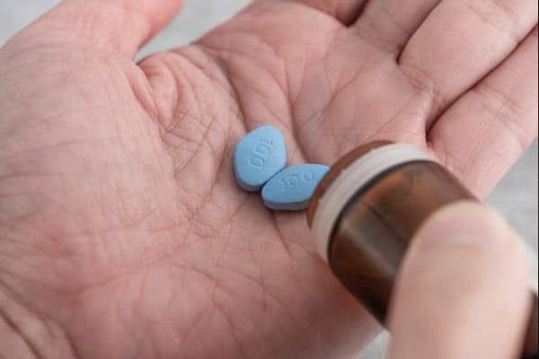 Eine Nahaufnahme einer Hand, die eine hellblaue Potenzpille hält, die im Artikel als Symptombehandlung thematisiert wird.