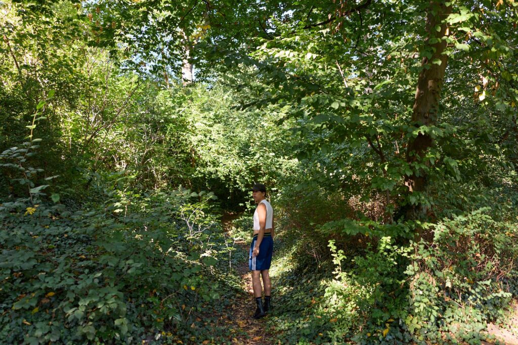 Man standing alone on a shady forest path - symbolic image for cruising in the woods, Grindr frustration and the search for thrills without dating apps.