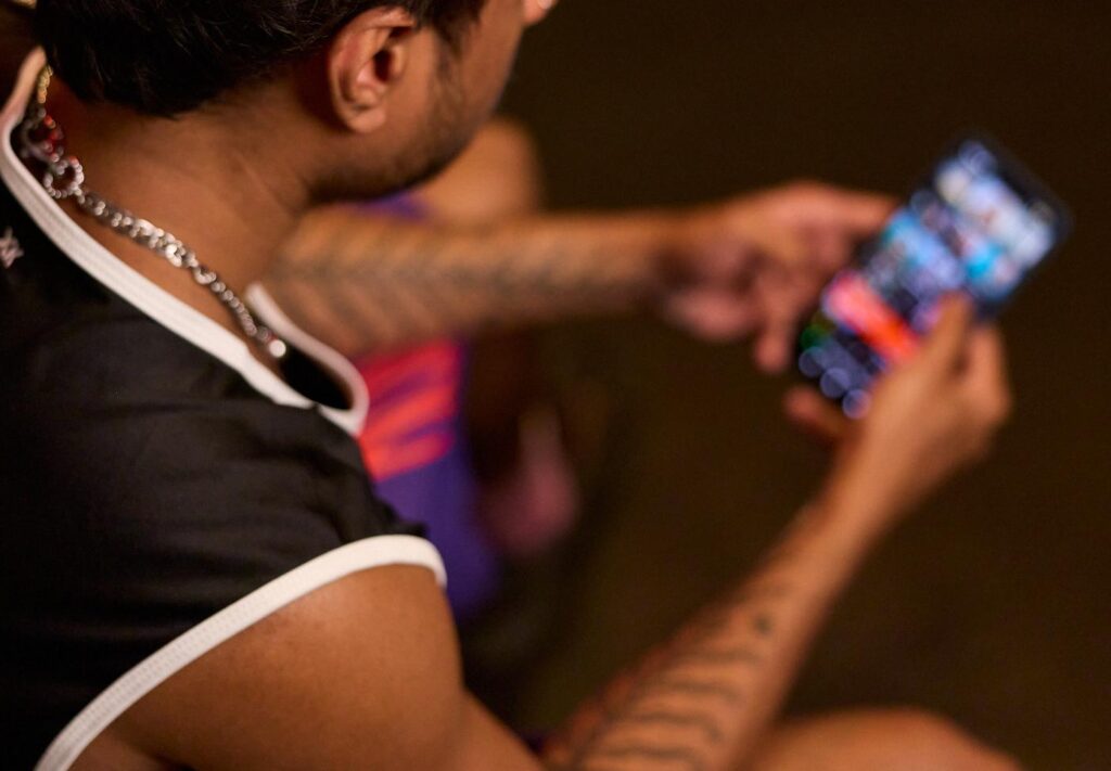Man sitting in the dark watching a dating app like Grindr on his smartphone - a symbolic image of how cruising in the woods and apps come together.