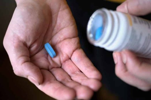 A person takes a tablet from a medicine container - symbolising protection through HIV therapy and safer sex.