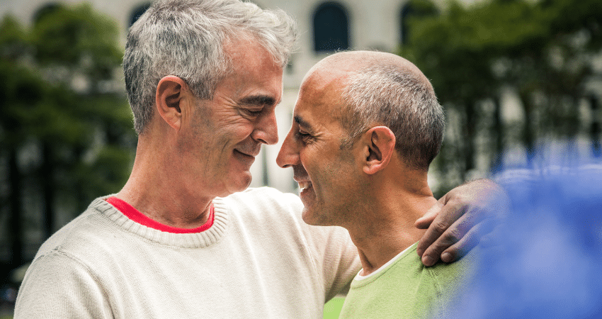 Zwei ältere Männer schauen sich liebevoll an und umarmen sich zärtlich.